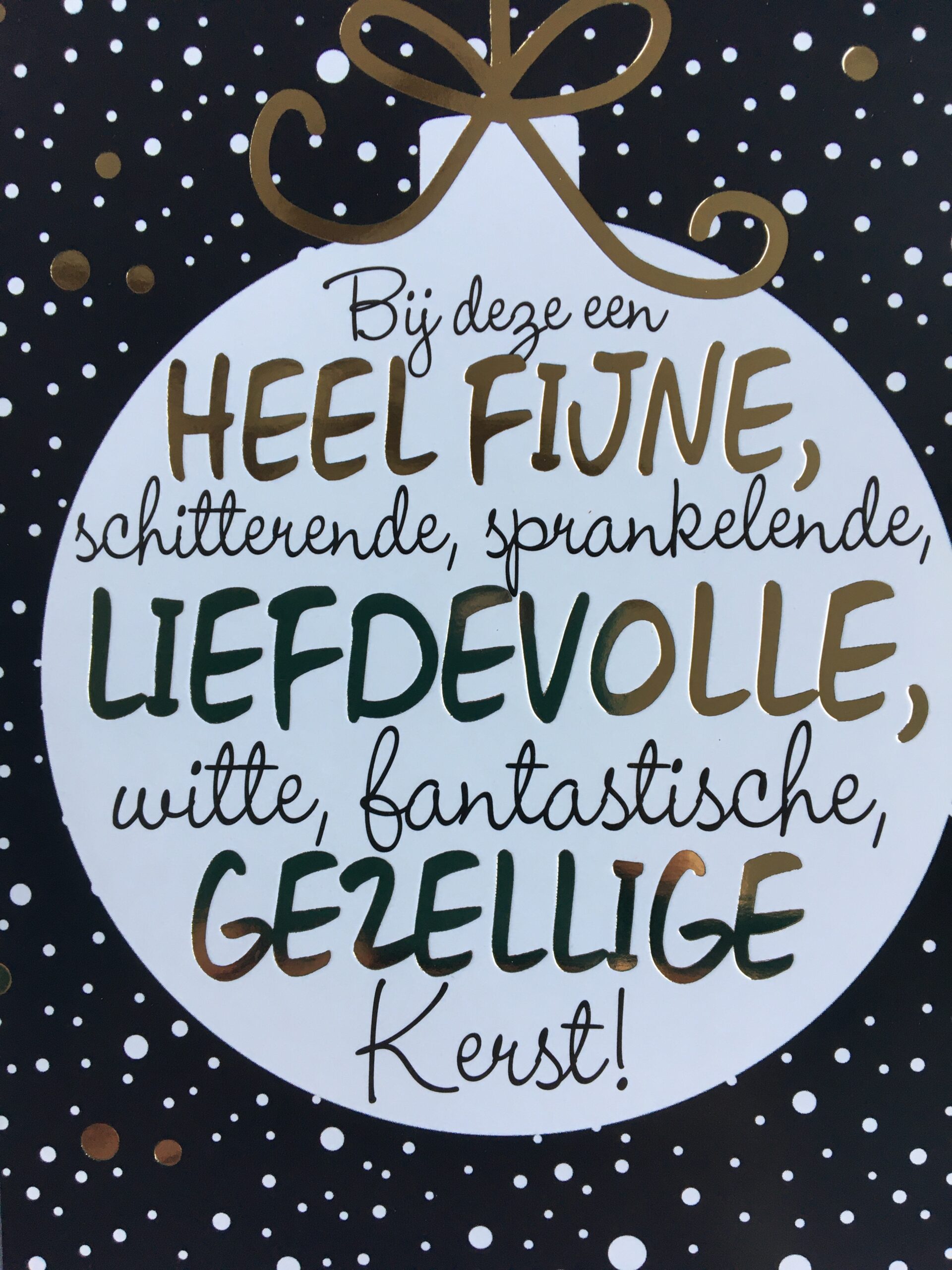 Op een donkere achtergrond met witte en gouden sneeuwvlokken staat een grote, witte kerstbal met een gouden strik. In de kerstbal staat "Bij deze een hele fijne, schitterende, sprankelende, liefdevolle, witte, fantastische, gezellige Kerst".